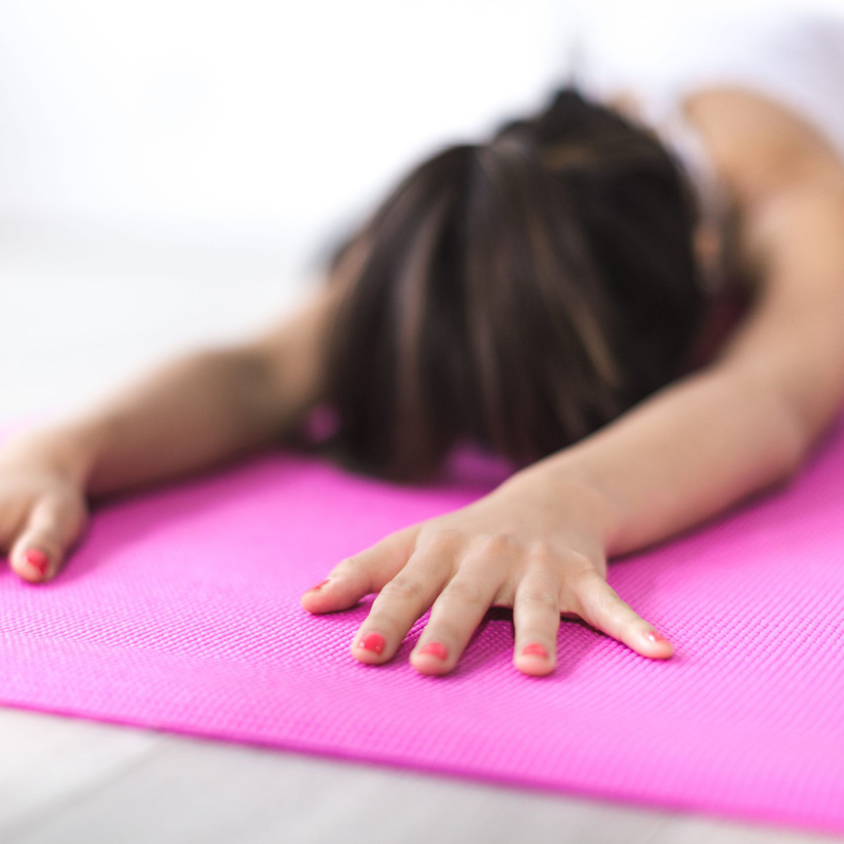 Woman stretches in child pose on a pink mat.